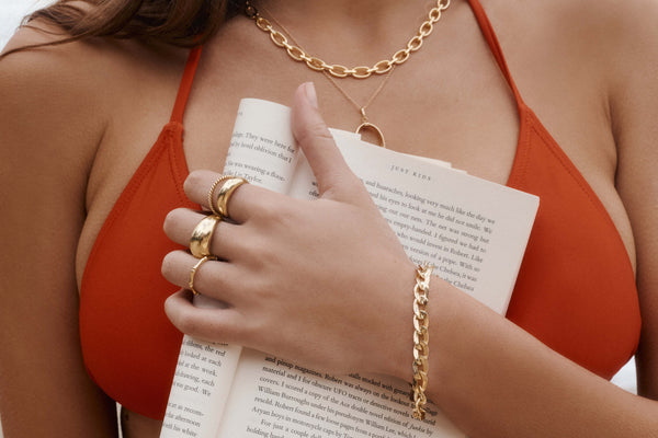Model wearing swimsuit and layered gold rings, bracelets and necklaces