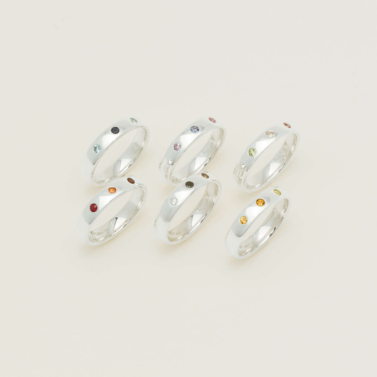 Six sterling silver Milestone Bands set with three gemstones each on a neutral background.