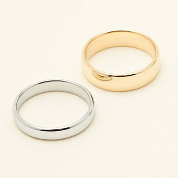Two plain metal bands, one silver and one yellow gold, photographed on a clean off-white background.