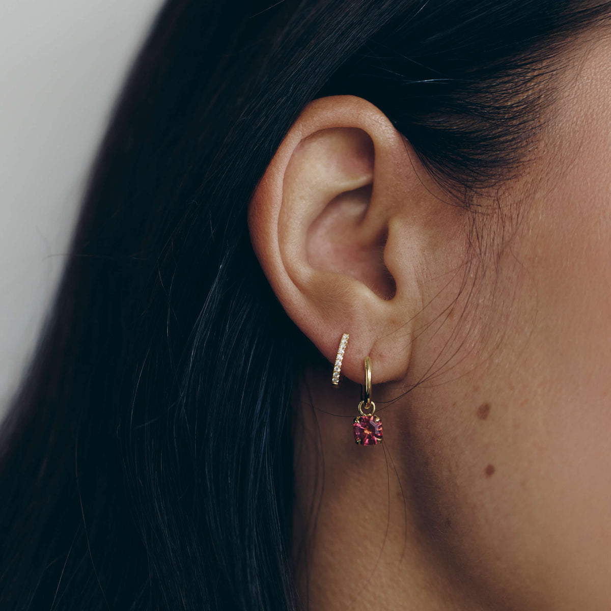Close-up of an ear wearing a gold hoop earring with a pink gemstone.